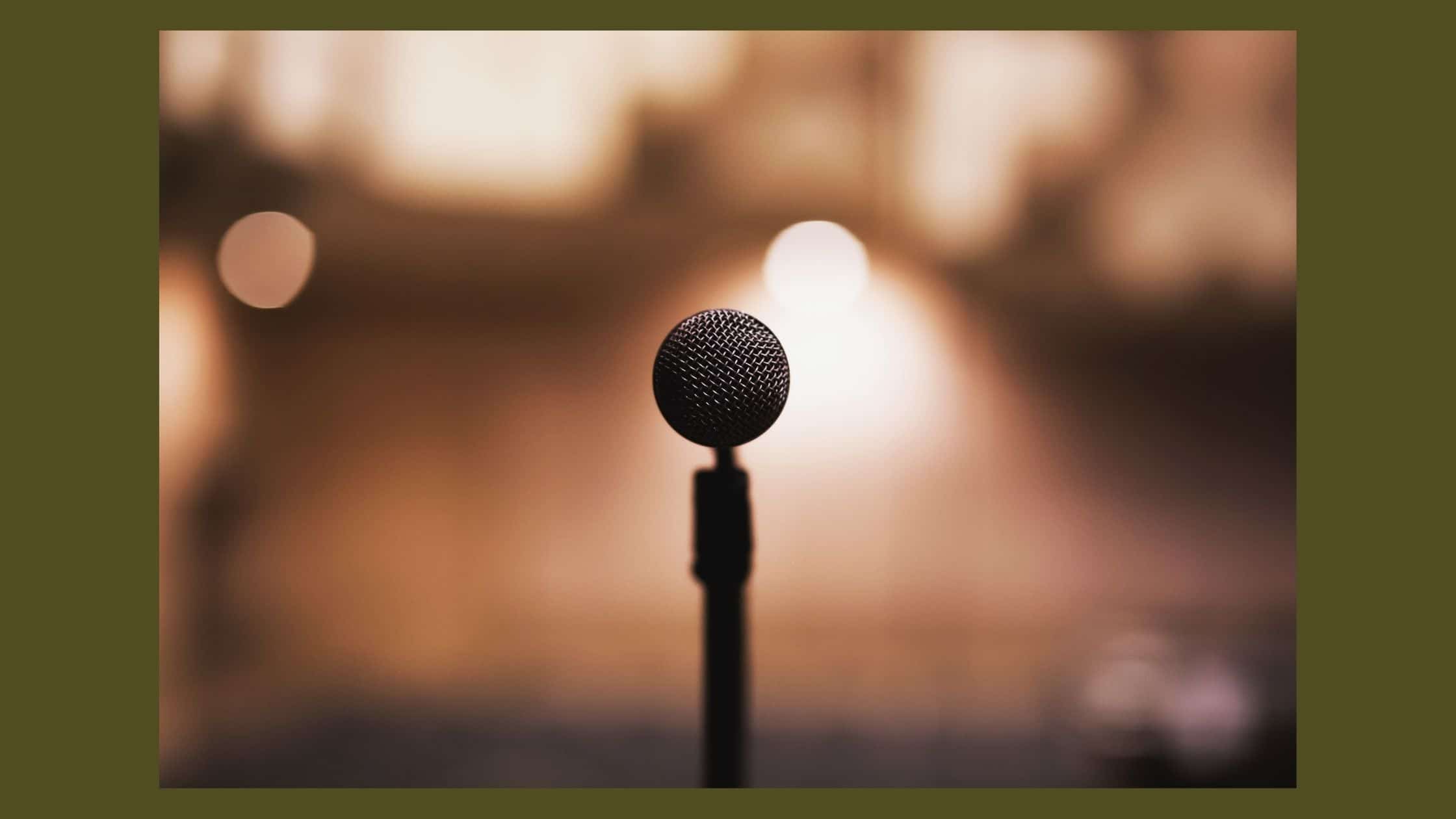 Een microfoon op een standaard vanuit de spreker gezien, op de achtergrond heel wazig een zaal.
