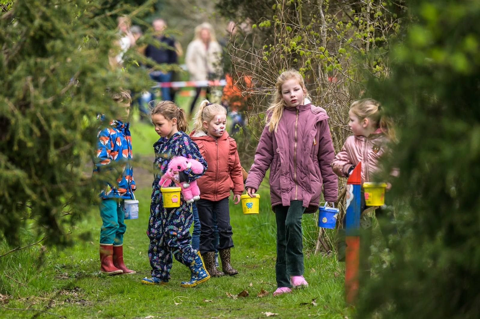 Een aantal kinderen staan kriskras op een velt met bomen op zoek naar eitjes.