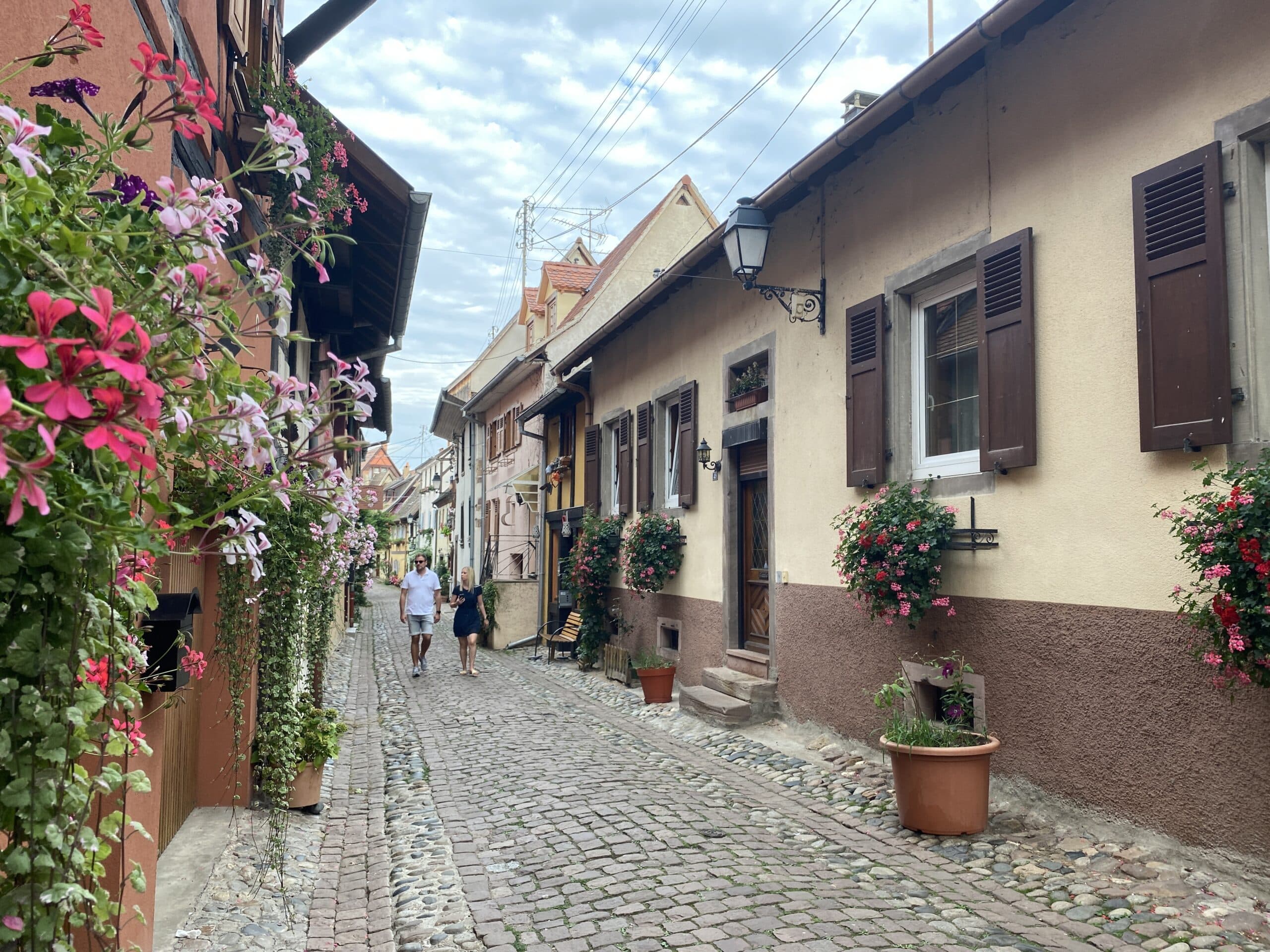 Een straat met kleurrijke huisjes, kasseien en bloemen.