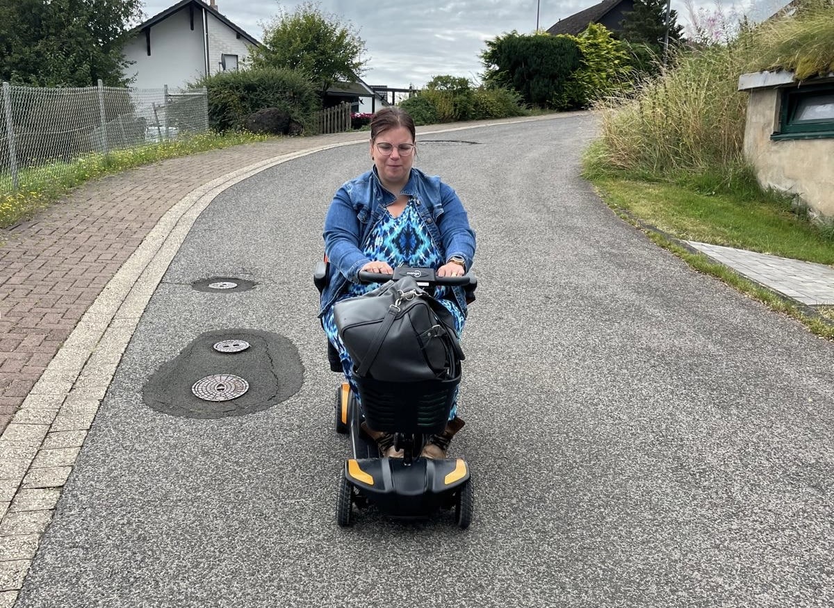 Joyce rijdt met haar scootmobiel over een weg.