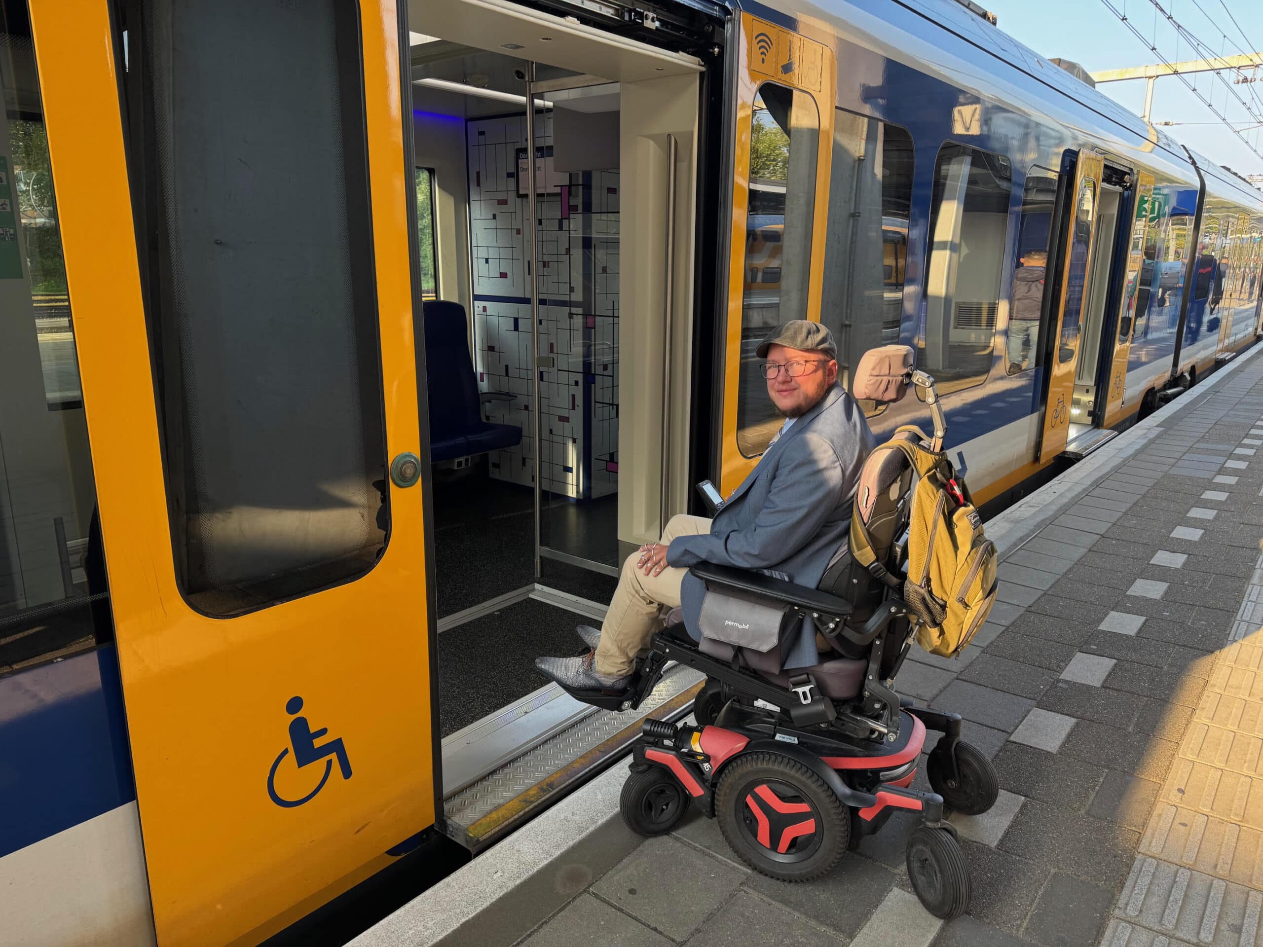 Nick staat in elektrische rolstoel voor sprinter met open deuren.