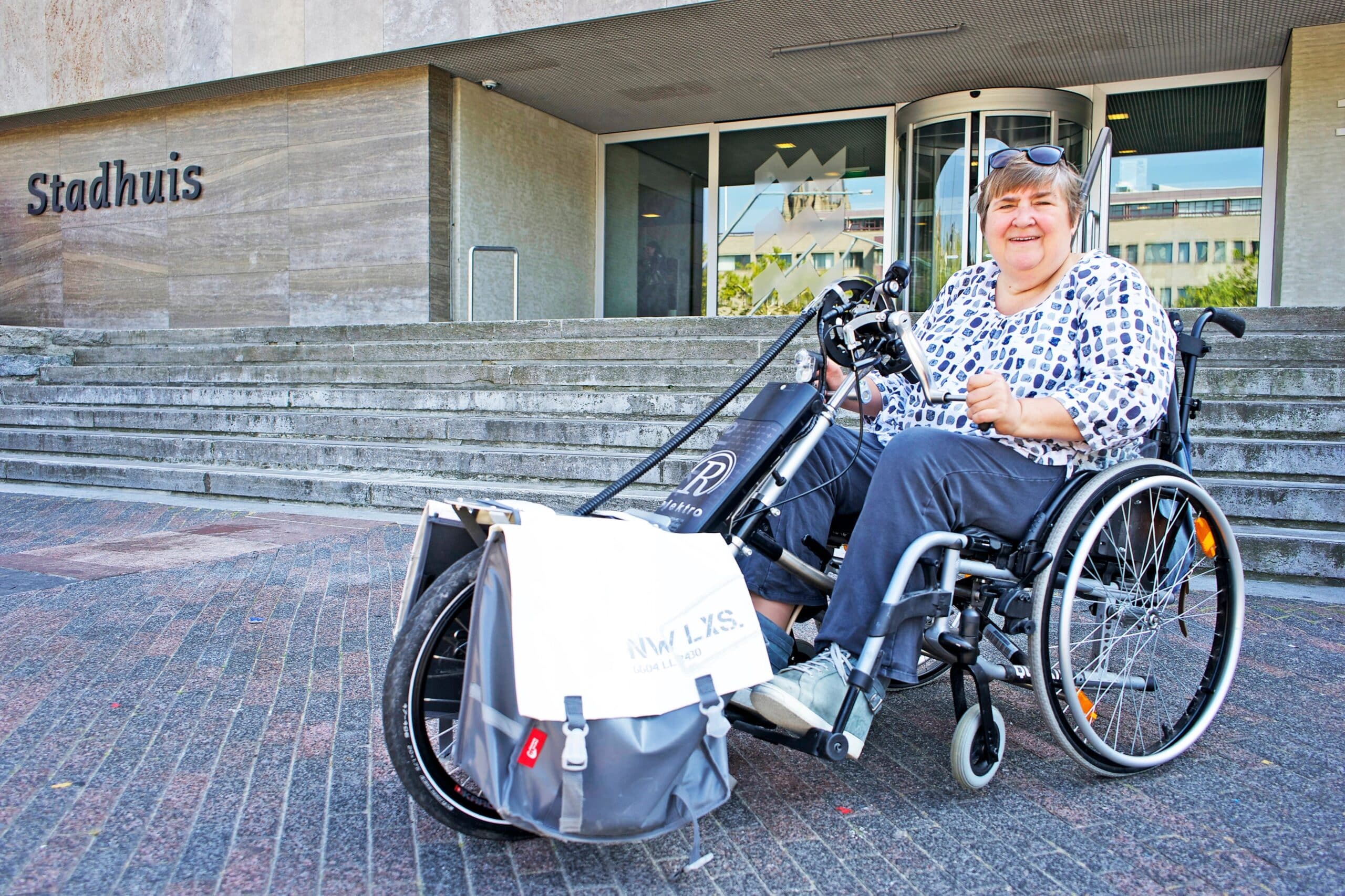 Pia poseert in tot handbike omgebouwde rolstoel voor een trap naar de entree van een stadhuis.