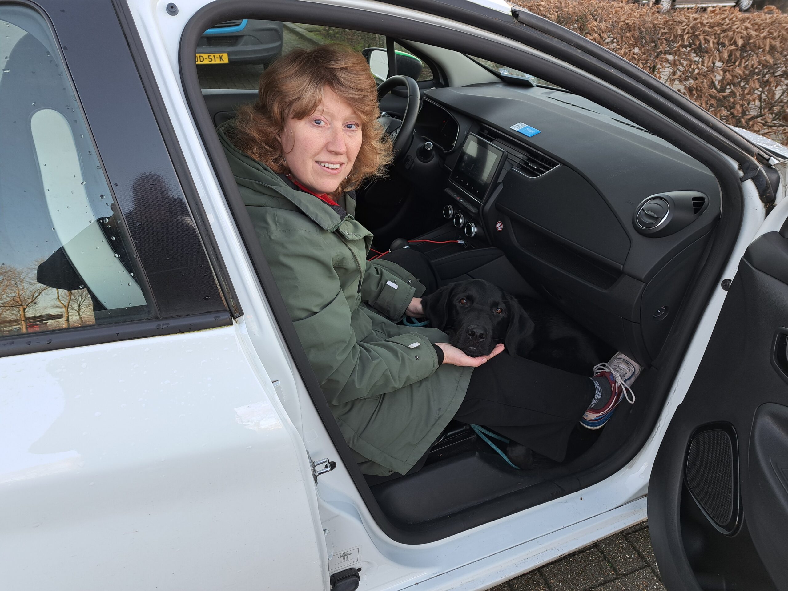 Martine van buiten de auto gefotografeerd terwijl ze met haar hond op de bijrijdersstoel zit.