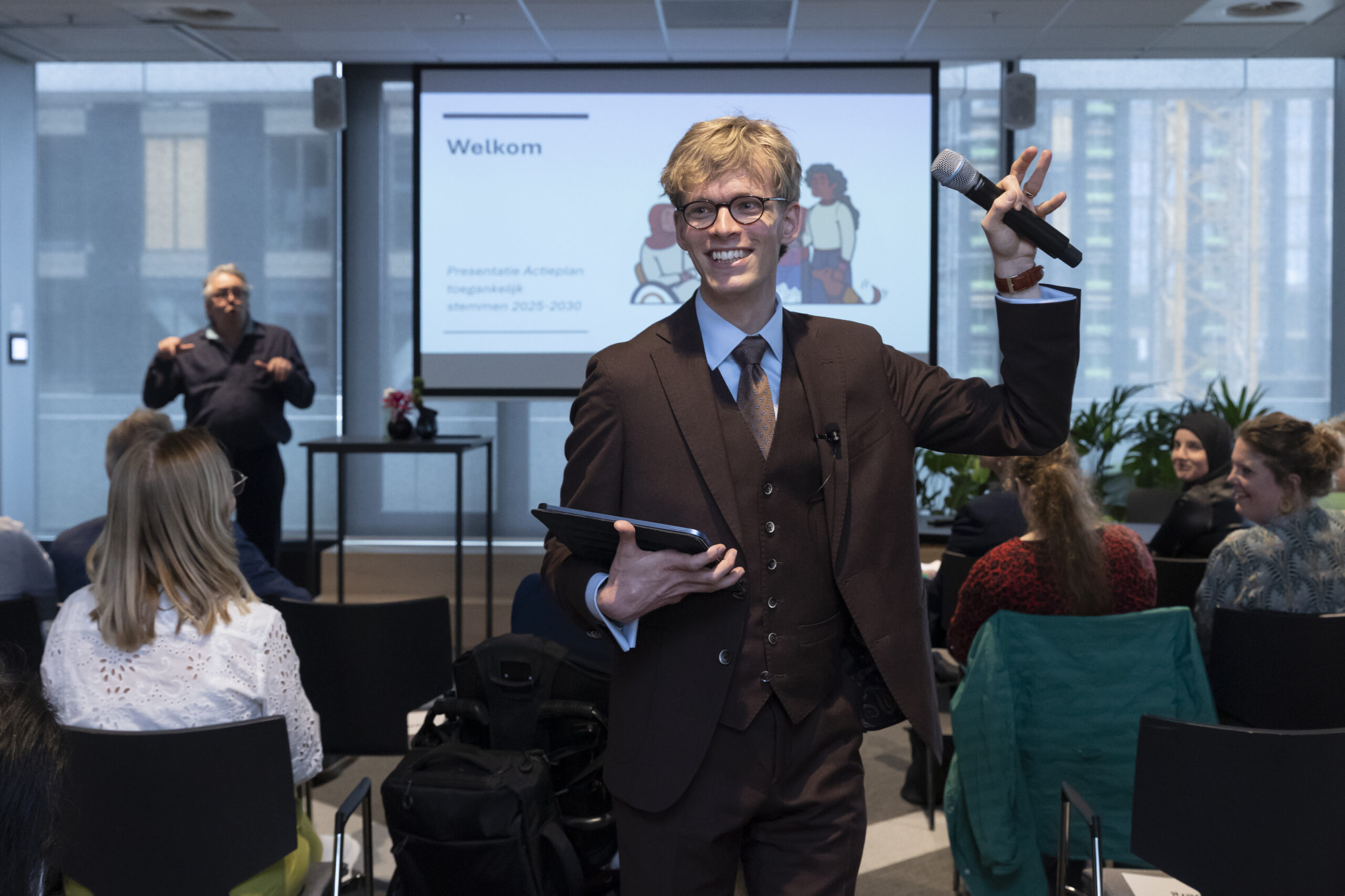 Ik sta in de zaal en hou een hand met een losse microfoon in de lucht.